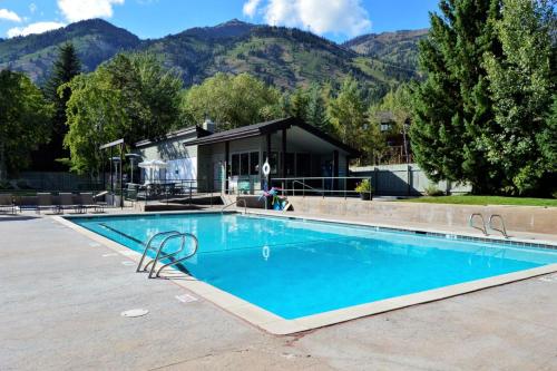 a swimming pool with a house and mountains in the background at RMR: Wind River 15 Condo in Teton Village in Teton Village