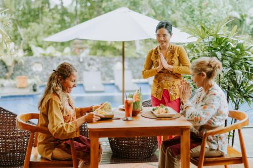 a woman sitting at a table with two daughters at Dewangga Suite in Ubud