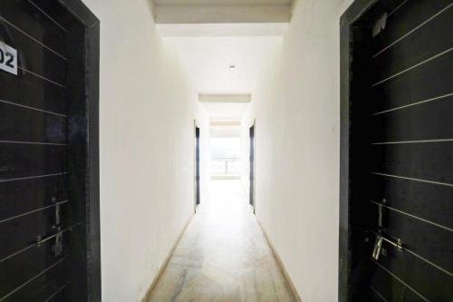 un couloir vide avec des murs blancs et des portes noires dans l'établissement Hotel O Raj Mahal, à Jabalpur