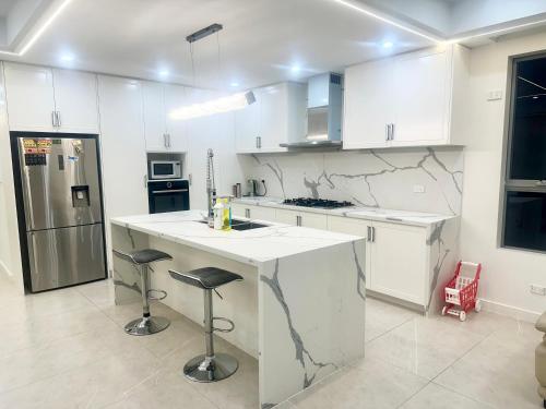a white kitchen with a counter and stools in it at Master room with Ensuite Near Train Station Airport in Revesby