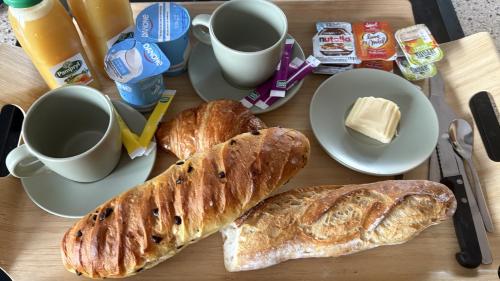 Una mesa cubierta con pan, croissants y tazas de café. en Une parenthèse verte, 