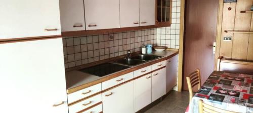 a kitchen with a sink and white cabinets and a table at Casa Checolongo in Ziano di Fiemme