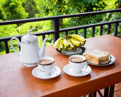 a table with two cups of coffee and a bunch of bananas at Mihidugiri Eco lodge in Kandy