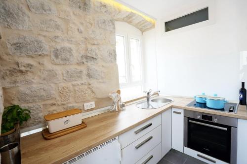 a kitchen with white cabinets and a stone wall at Contarini Apartment in Split