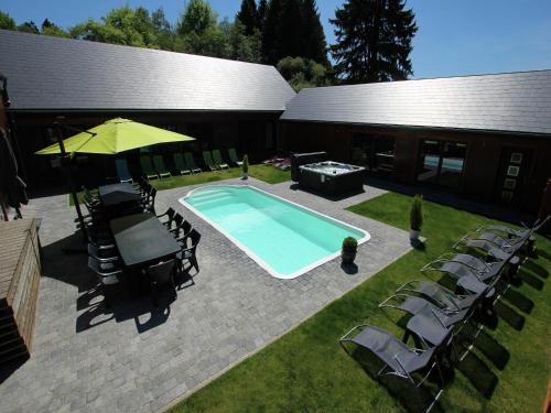 una piscina con sillas y una sombrilla junto a un edificio en Villa with heated outdoor pool and sauna, en Manhay