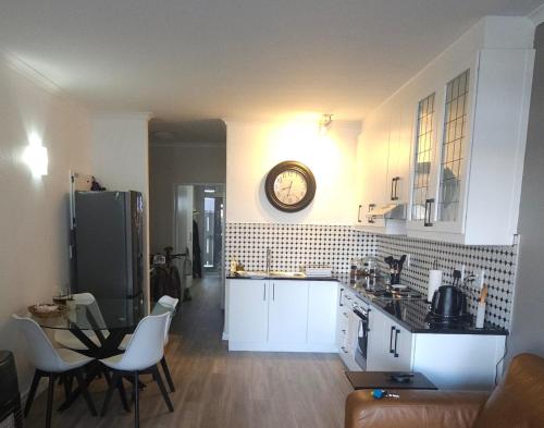 een keuken met witte kasten en een klok aan de muur bij Seaside Charm in Bloubergstrand