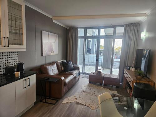 een woonkamer met een bank en een keuken met een raam bij Seaside Charm in Bloubergstrand