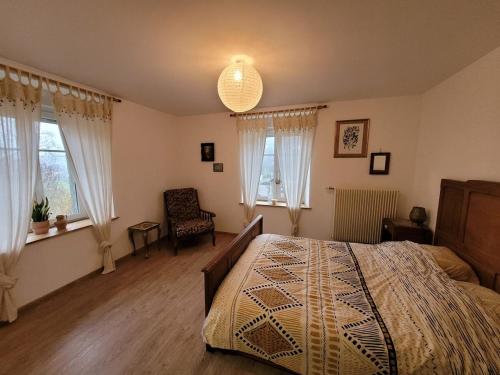 a bedroom with a bed and a chair and windows at Gîte cosy dans les Vosges in Rochesson