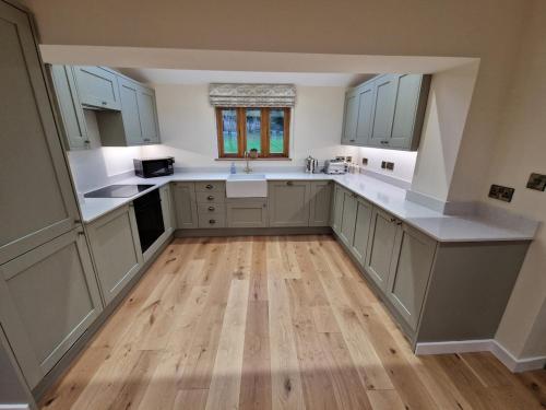 a kitchen with white cabinets and a wooden floor at Malthouse Barn, Staffordshire in Gnosall