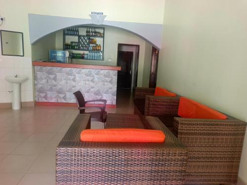a room with wicker furniture and a bar with orange pillows at Guardian Motel Kasese in Kasese