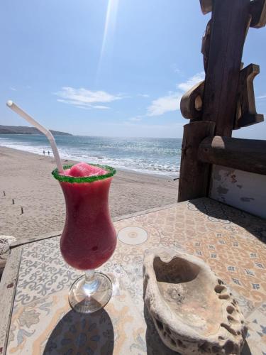 a drink in a glass sitting on a table at the beach at Máncora Hostel Restocafebar in Máncora