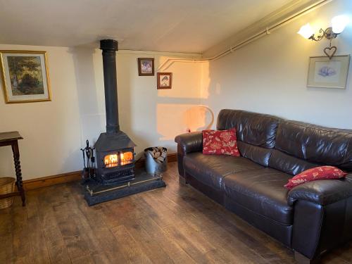a living room with a leather couch and a wood stove at The Old Barn in Bettws Gwerfil Goch