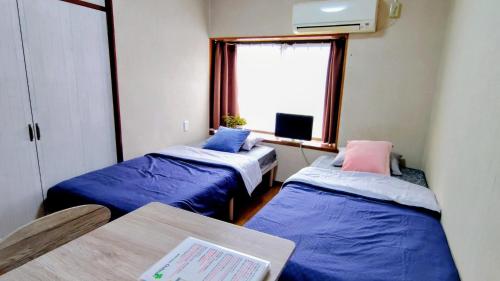 twee bedden in een kamer met een tafel en een raam bij Kokusaigakusya Ozukikaikan - Vacation STAY 18798 in Hadano