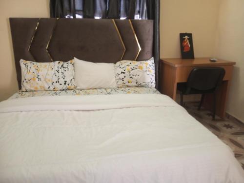 a bed with white sheets and pillows next to a desk at Richbee Hotel and Suites in Abuja