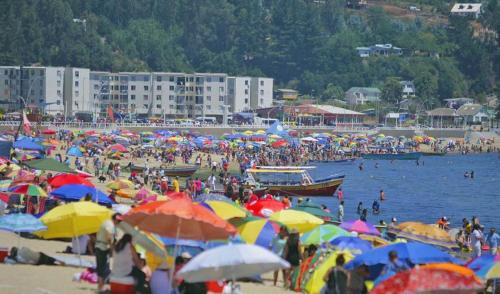 a crowd of people on a beach with umbrellas at Departamento Dichato hasta 7 personas frente a la playa in Dichato