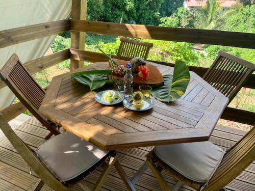a wooden table with a plate of food on a deck at Lodges atypiques, filet suspendu ou lit mobile pour expérience unique sous les etoiles in Petit-Bourg