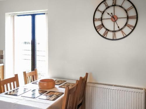 une table à manger avec une grande horloge sur le mur dans l'établissement Russet Cottage - E4678, à Lympsham