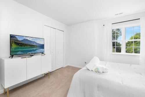 a white bedroom with a flat screen tv on a wall at Stylish Queen City Getaway in Camp North End in Charlotte