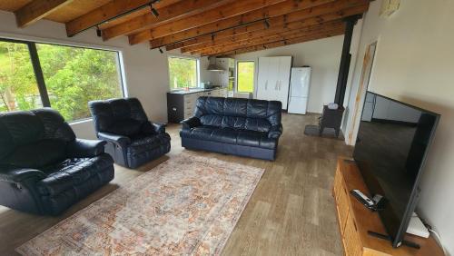 sala de estar con 2 sillas de cuero y TV de pantalla plana en Paradise HQ Pukenui, en Pukenui