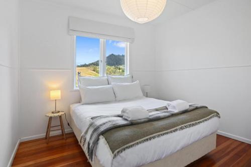 ein weißes Schlafzimmer mit einem Bett und einem Fenster in der Unterkunft The Beach Cottage - Close to Beach and Town in Tairua