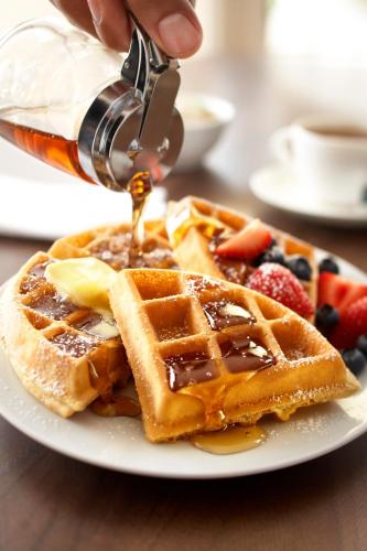 a person is pouring syrup onto a plate of waffles at Country Inn & Suites by Radisson, Gettysburg, PA in Gettysburg