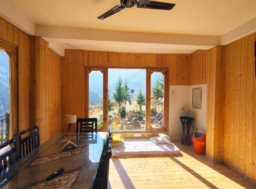 a room with wooden walls with a table and a large window at The VOID - Tirthan Valley in Gushaini