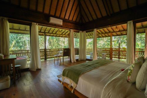 a bedroom with a large bed and large windows at The Shala Bali in Ubud