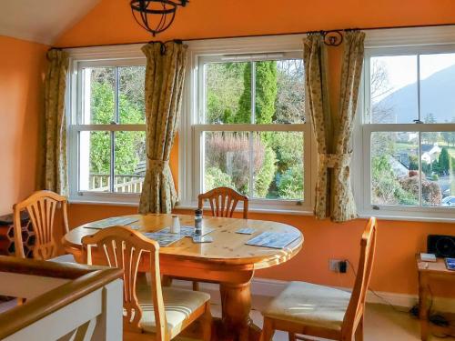 a dining room with a table and two windows at Thwaite Hill Cottage in Braithwaite
