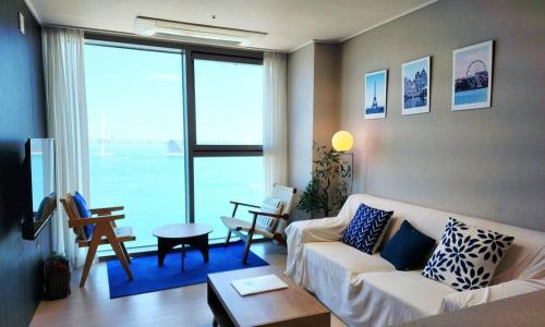 a living room with a white couch and a large window at an emotional view of the sea at sunrise in Kwangan-dong