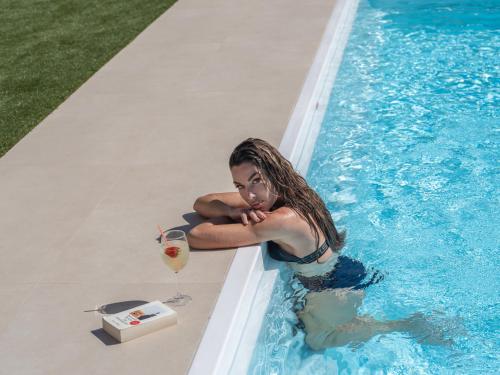 una mujer sentada en una piscina con una bebida en Arhontiko Arhanes Suites, en Archanes
