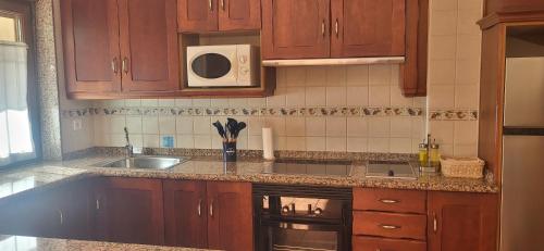 eine Küche mit Holzschränken, Spüle und Mikrowelle in der Unterkunft La Casa de la Vega in Las Arenas