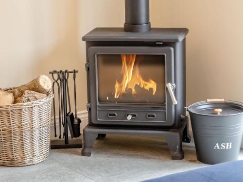 Una estufa de leña en una sala de estar con una canasta. en Dip Tub Den - Uk35989, en Wansford