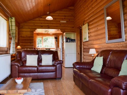 a living room with leather furniture in a log cabin at Fingask Log Cabin - S4394 in Glenfarg