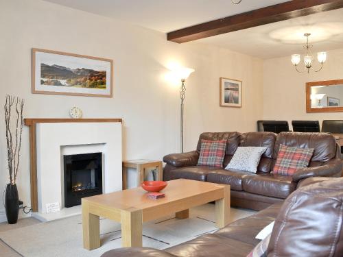 a living room with a leather couch and a fireplace at School Knott Cott in Windermere
