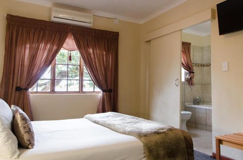 a bedroom with a bed and a window and a bathroom at Nelspruit Lodge in Nelspruit