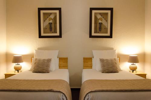 two beds in a hotel room with two lamps at Nelspruit Lodge in Nelspruit