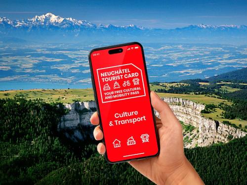 Una persona sosteniendo un teléfono celular rojo frente a una montaña. en Charmettes, en Neuchâtel