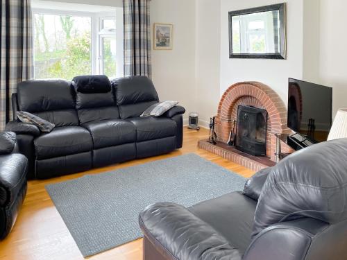 a living room with a leather couch and a fireplace at Beacon Cottage in Ivybridge