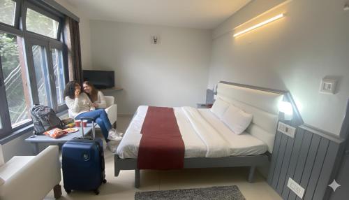 two women sitting in a room with a bed at Hotel Sunrise Meadows Mountain in Manāli