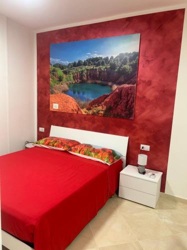 a bedroom with a red bed with a painting on the wall at Masseria Causio in Giurdignano