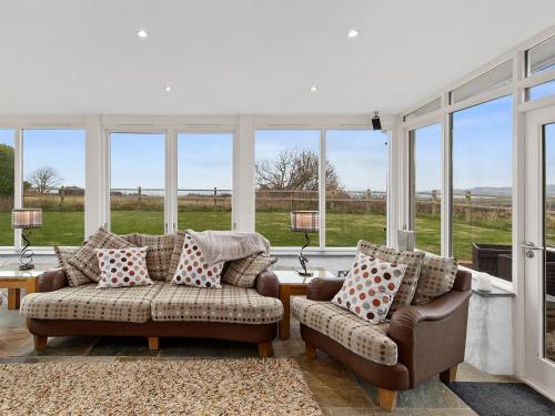 ein Wohnzimmer mit 2 Stühlen, einem Sofa und Fenstern in der Unterkunft Temple Barn in Abercastle