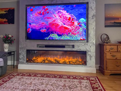 a living room with a fireplace with a tv above it at Rivendell Lodge - Cottage in East Winch