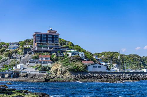 a building on top of a hill next to the water at Ocean View Hiromi SPA Hotel温泉と絶景の宿 in Shimoda