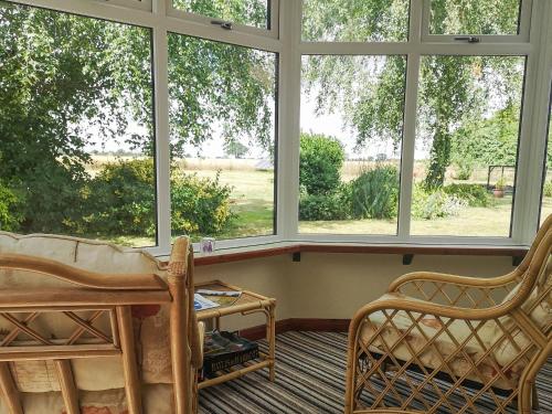 a room with two chairs and a table and windows at Elm Barn View in Freethorpe