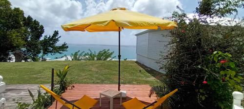een gele parasol en stoelen op een patio bij "Studio Bellevue" Terrasse et Deck vue mer-Accès piscine in Le Diamant