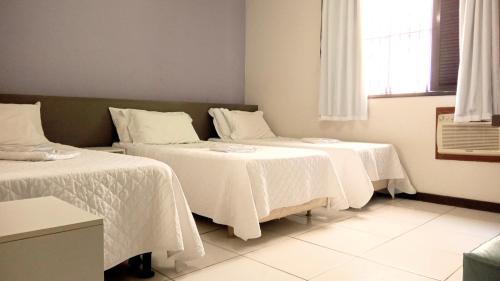 a room with two beds with white sheets and a window at Pousada Colonial in Macaé