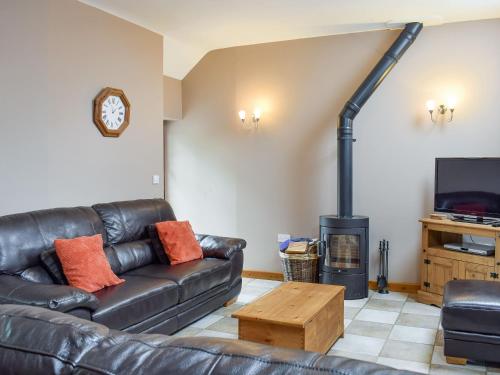 a living room with a leather couch and a wood stove at The Granary- Osc in Penbryn