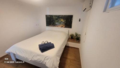 Un dormitorio pequeño con una cama blanca y un maletín negro encima. en Beit Nofesh, en Tiberíades