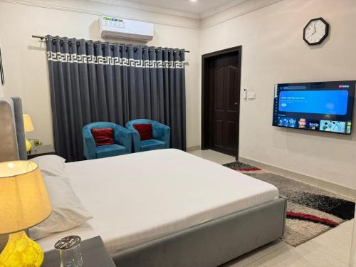 a room with a bed and two chairs and a tv at Cozy & Peaceful Rooms Near Lyallpur Galleria in Faisalabad