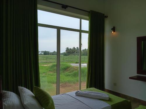 - une chambre avec une grande fenêtre donnant sur un champ dans l'établissement Paddi Breeze Cottage - Yala Safari, à Lukasgoda